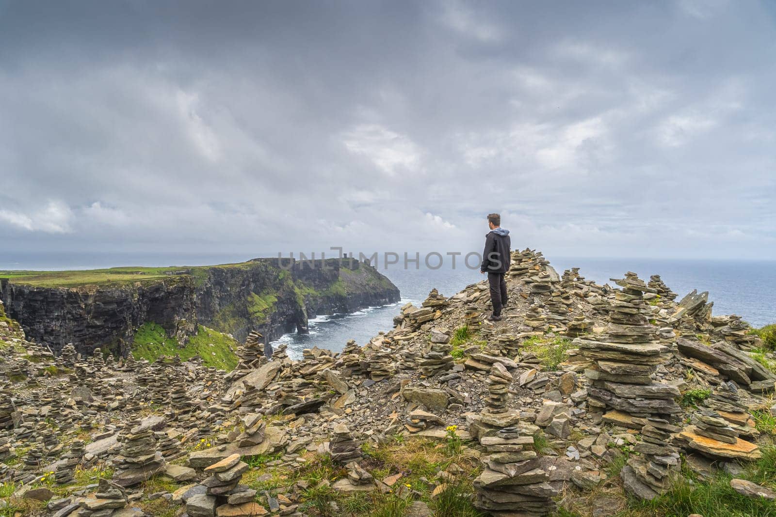 Man standing between stone stackings and admiring view on in iconic Cliffs of Moher, popular tourist attraction, Wild Atlantic Way, Co. Clare, Ireland
