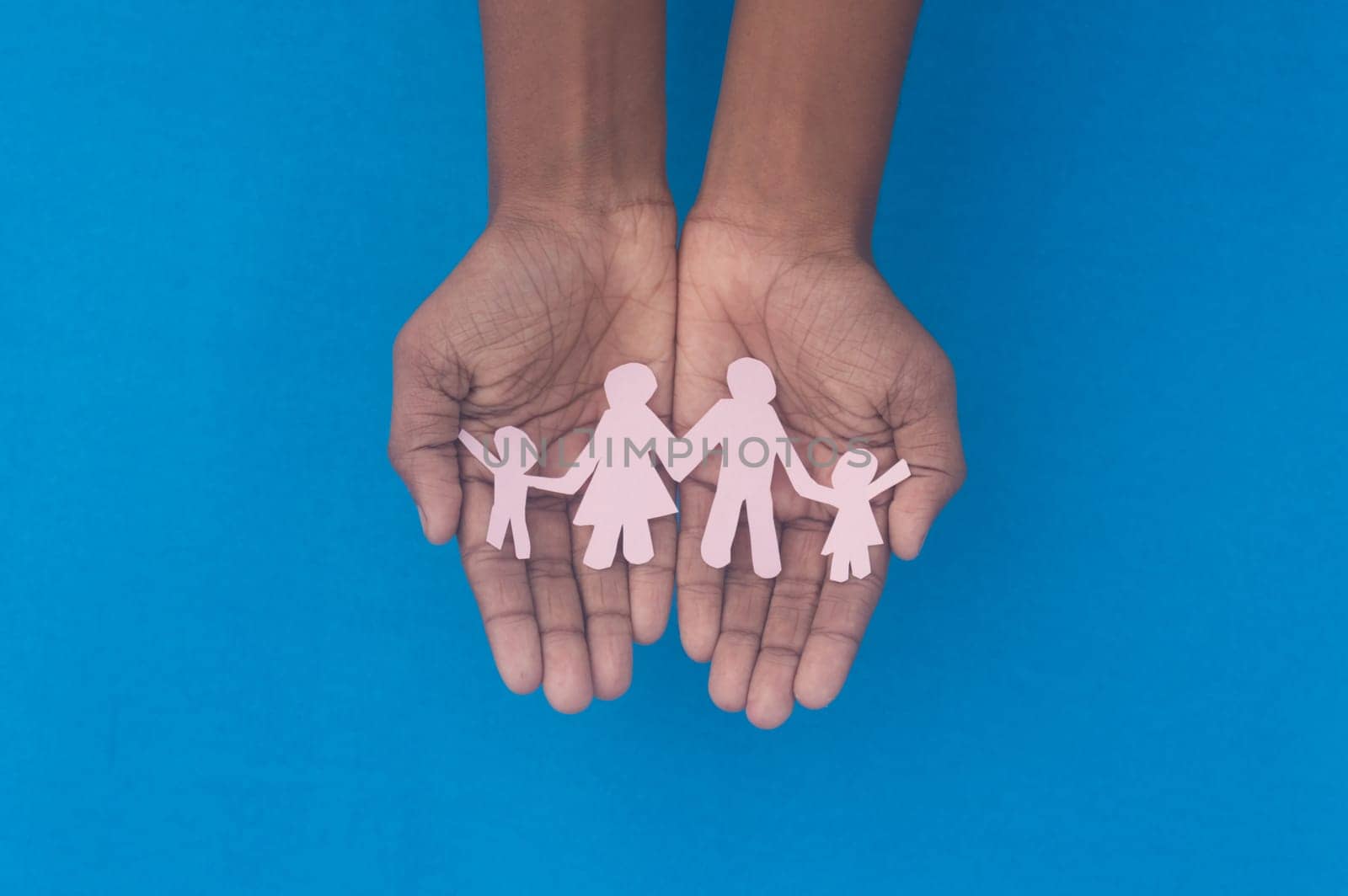 Hand holding family figure cutout top view. World health day Protection against domestic violence, healthcare and medical background. Foster care, homeless support and social distancing concept.