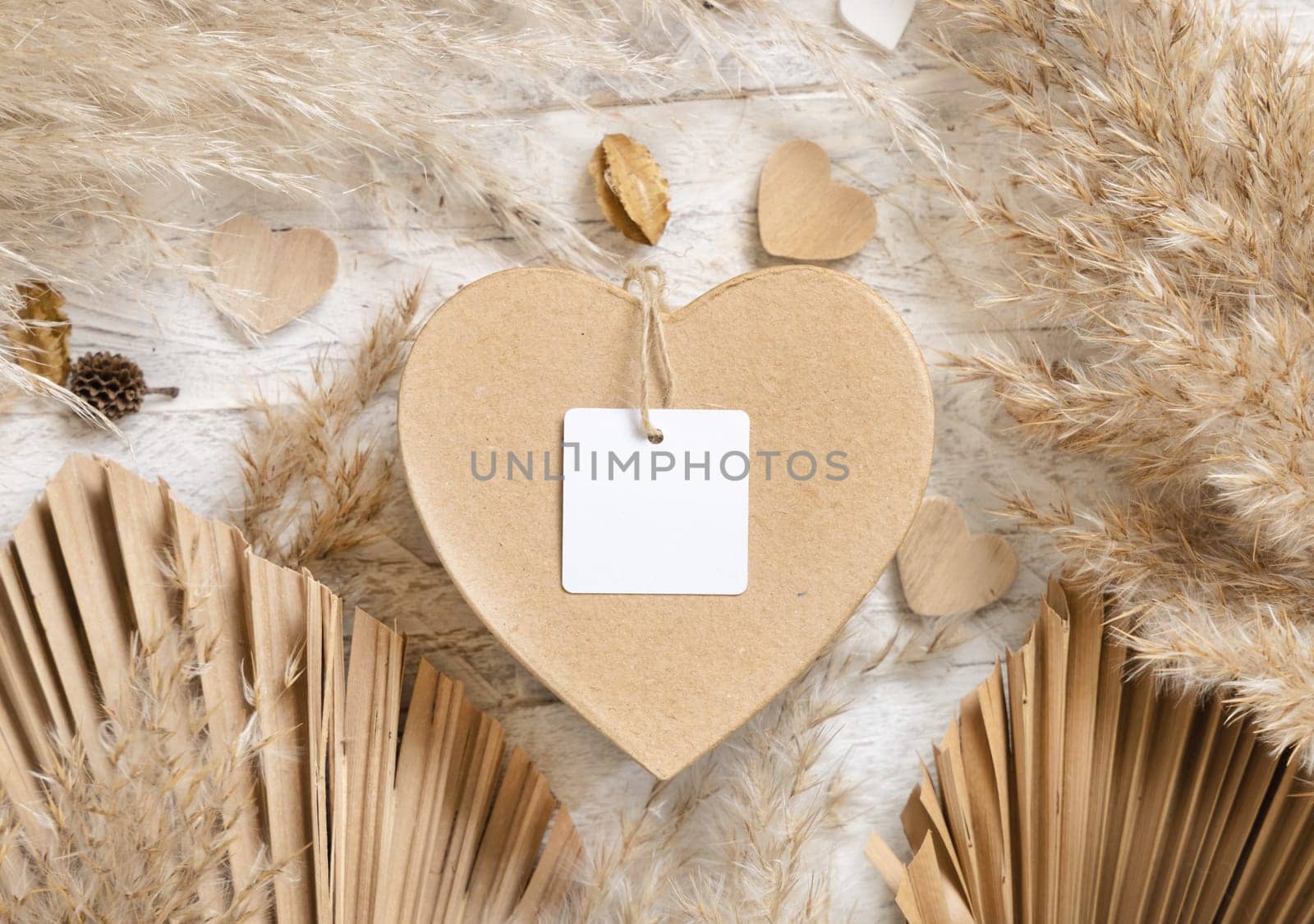 Heart shaped Valentines present with square blank gift tag near dried pampas grass, palm leaves and hearts top view. Rustic, cottage chic or bohemian label mockup, copy space