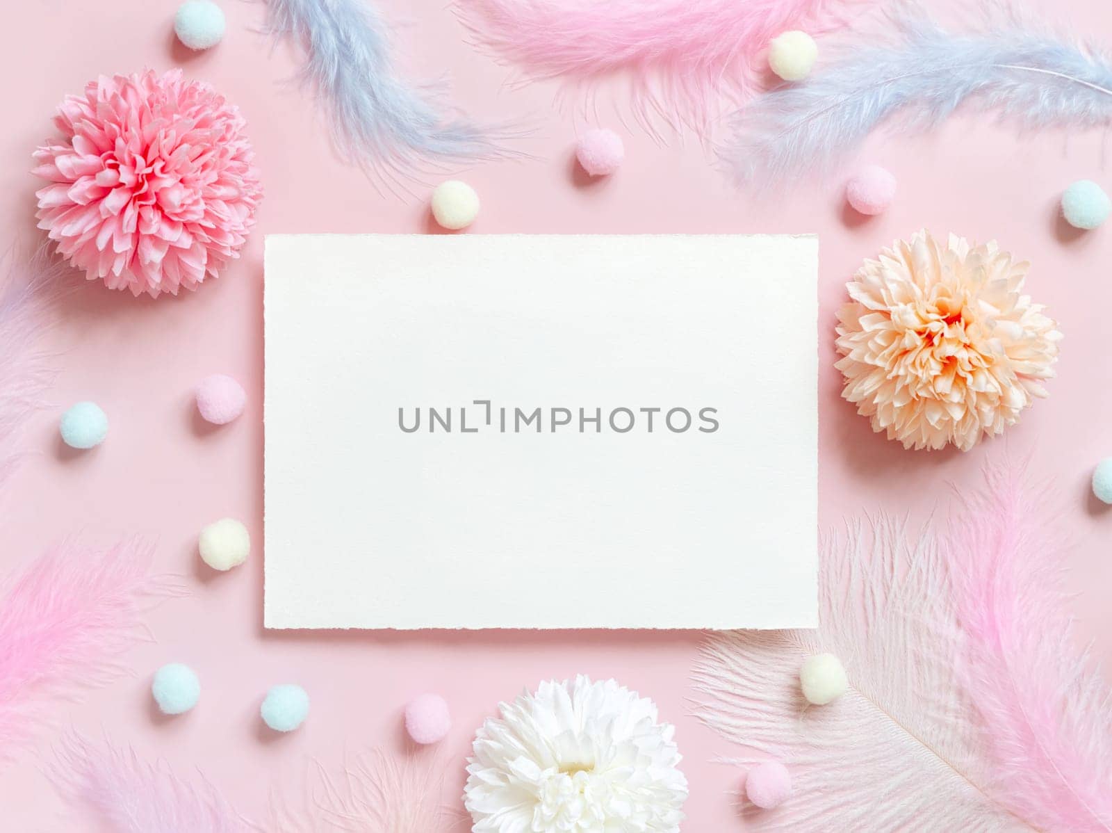 Blank card between pastel flowers, pom-poms and feathers near ring in a gift box on pink top view. Romantic scene with horizontal paper card with place for text flat lay. Valentines, Spring or girlish concept