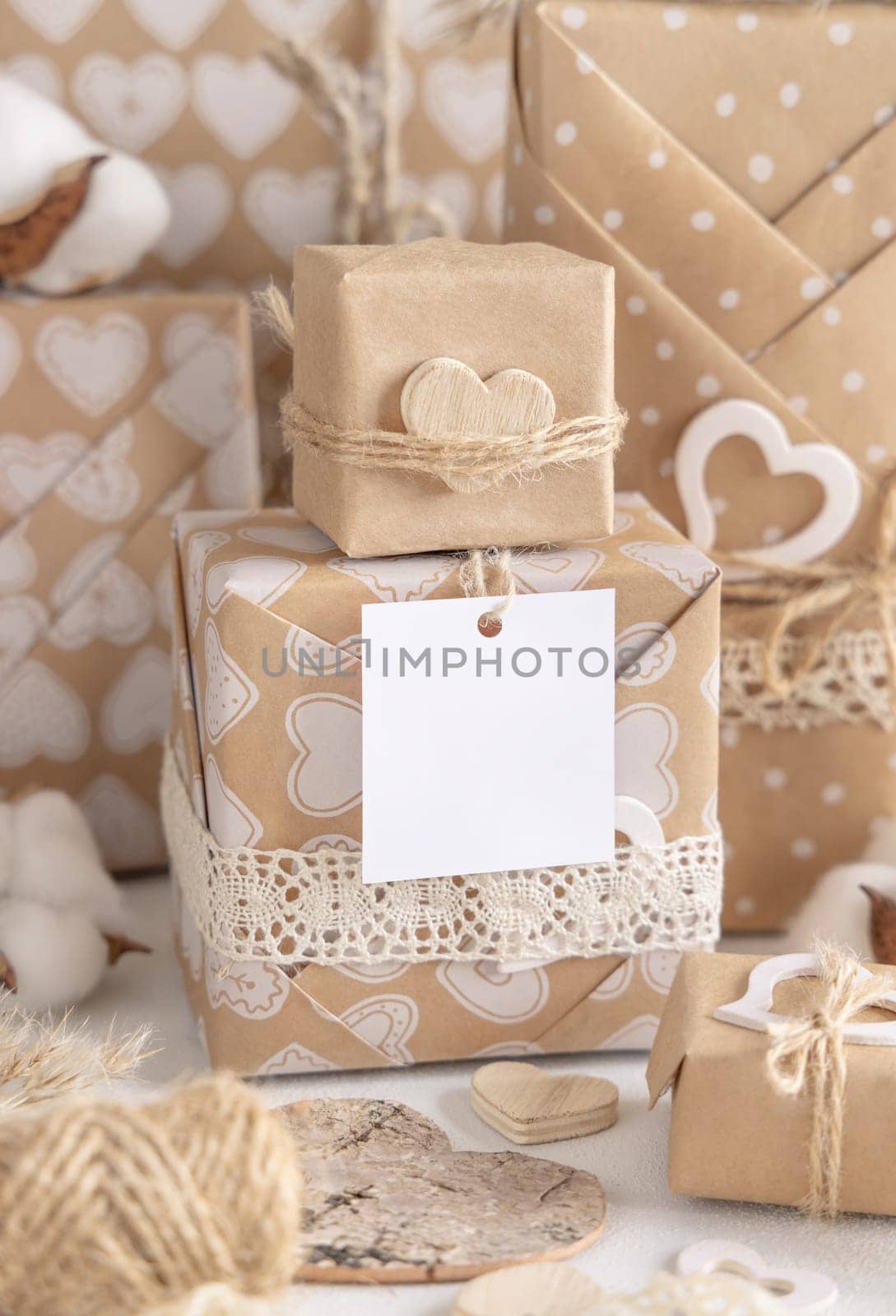 Valentines kraft paper wrapped presents with square gift tag and hearts close up. Spring scene with blank label. Rustic, cottage chic or bohemian mockup, copy space