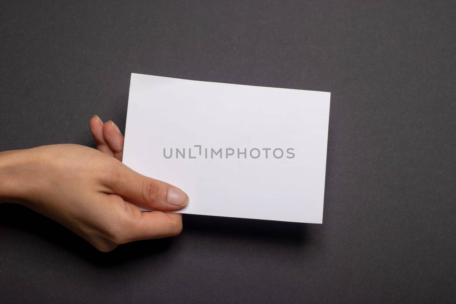 female hand holds a blank piece of paper with copy space in front of a black background cardboard