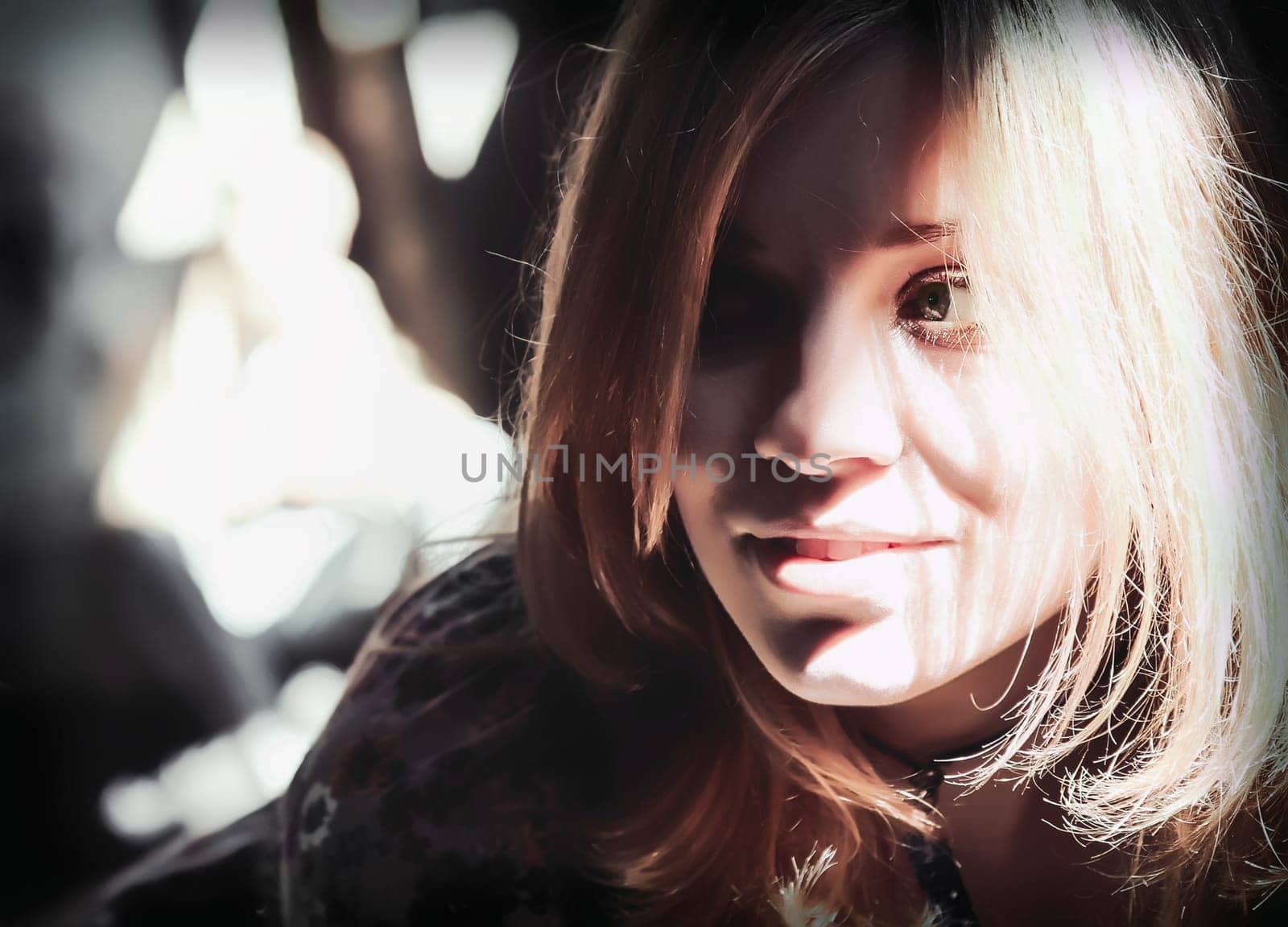Bright sunlight through the window illuminated the smiling face of an attractive young blond woman. Portrait headshot with shallow depth of field, contrasting shadows, soft selective focus.