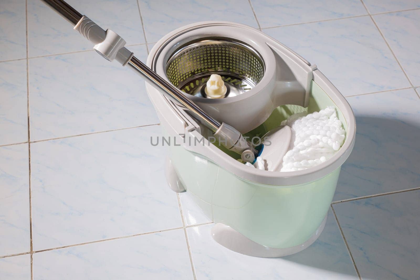Mop with microfiber head spinning on the bucket next to floor cleaning liquid and mopping the floor house in the living room