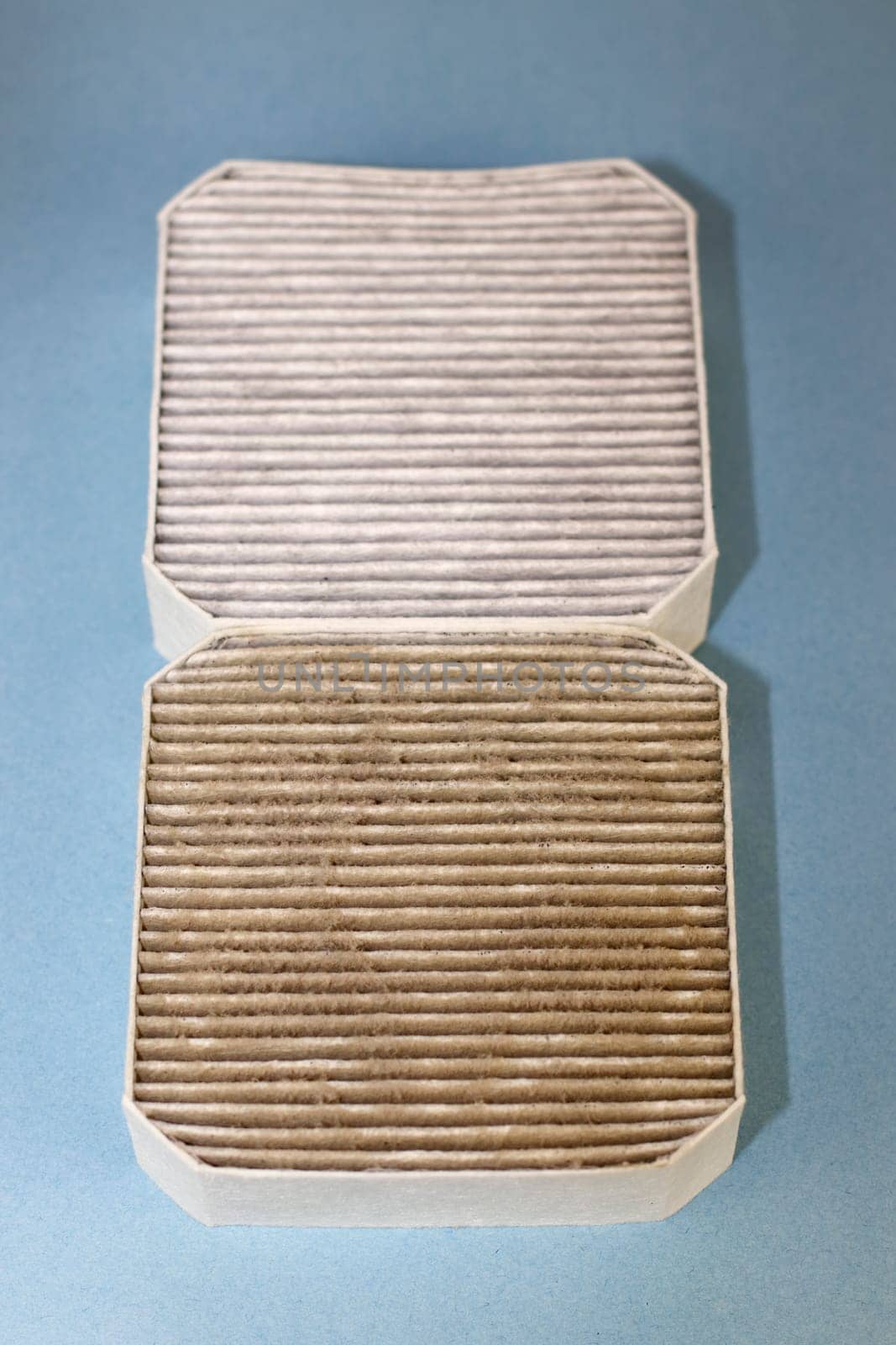 Two small square air filters that are also pre-filters, one dirty closer to viewer and one clean on a light blue background. One dirty air filter filled with dust, allergens and dirt under a clean one