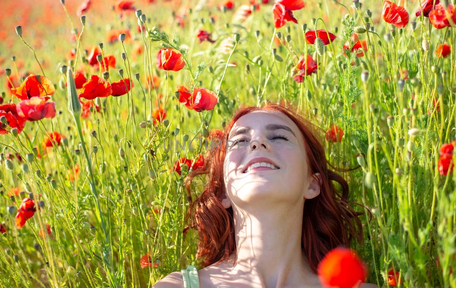 girl with red hairs lying in poppy field