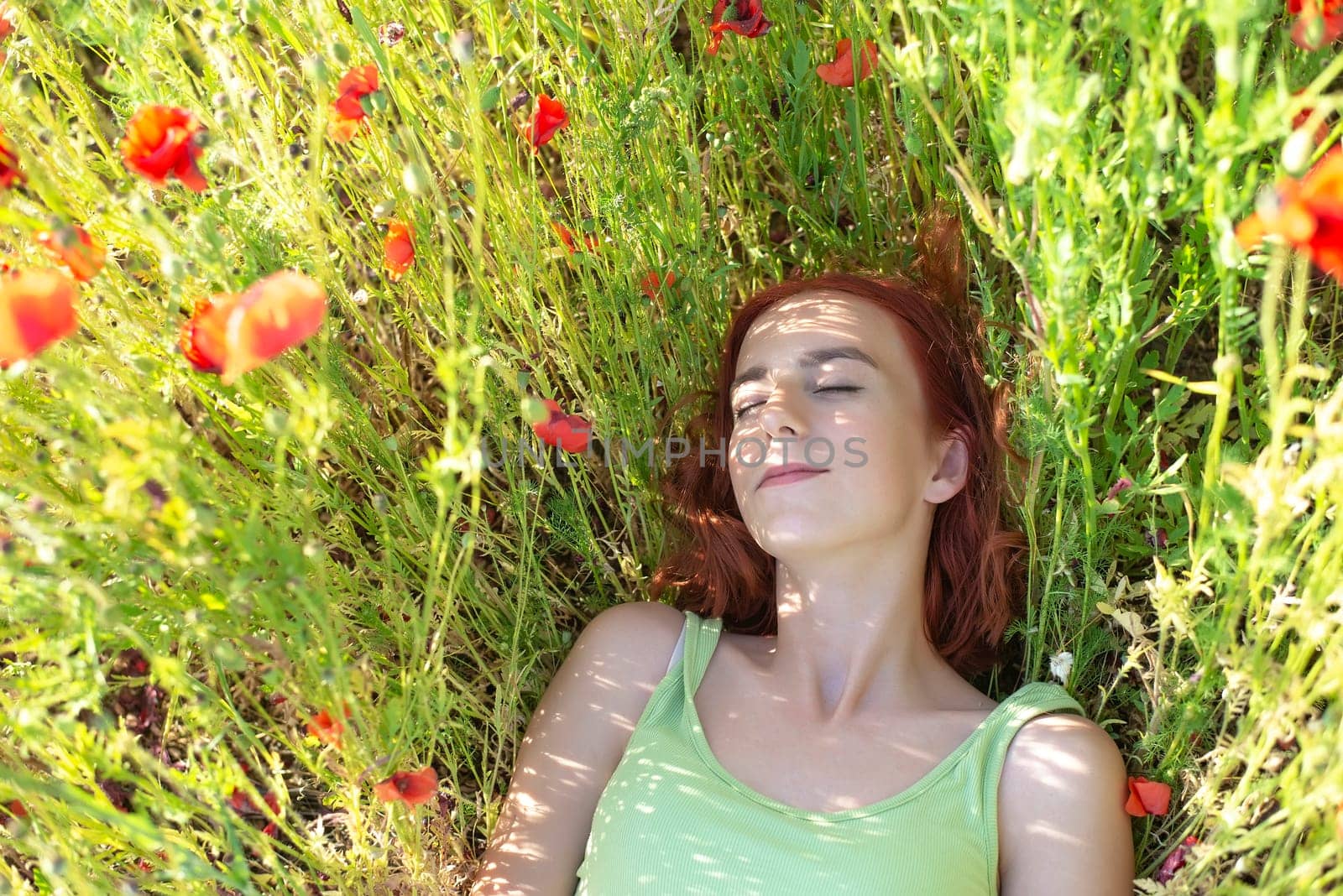 girl with red hairs lying in poppy field