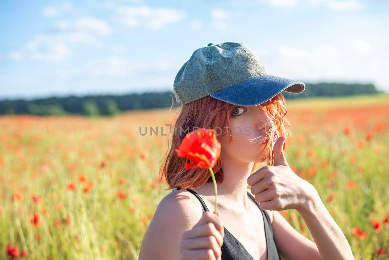 smiling young girl with poppy flower showing thumb up
