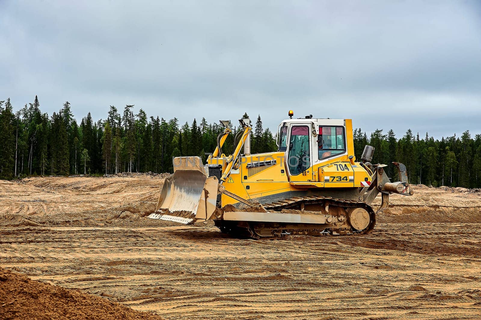 A yellow tractor bulldozer stands in a sand pit. High quality photo