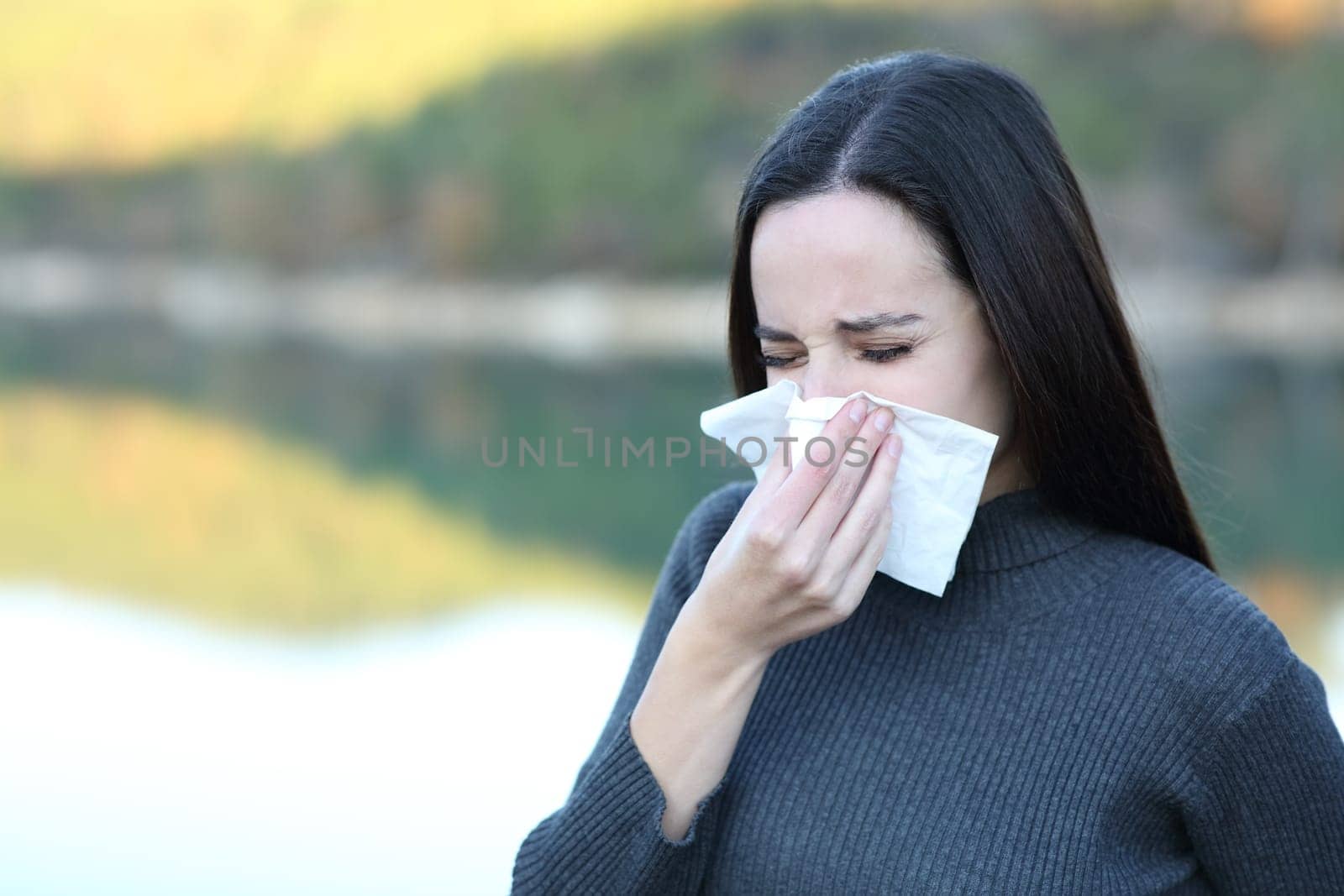 Ill woman blowing nose with a tissue outdoors in winter