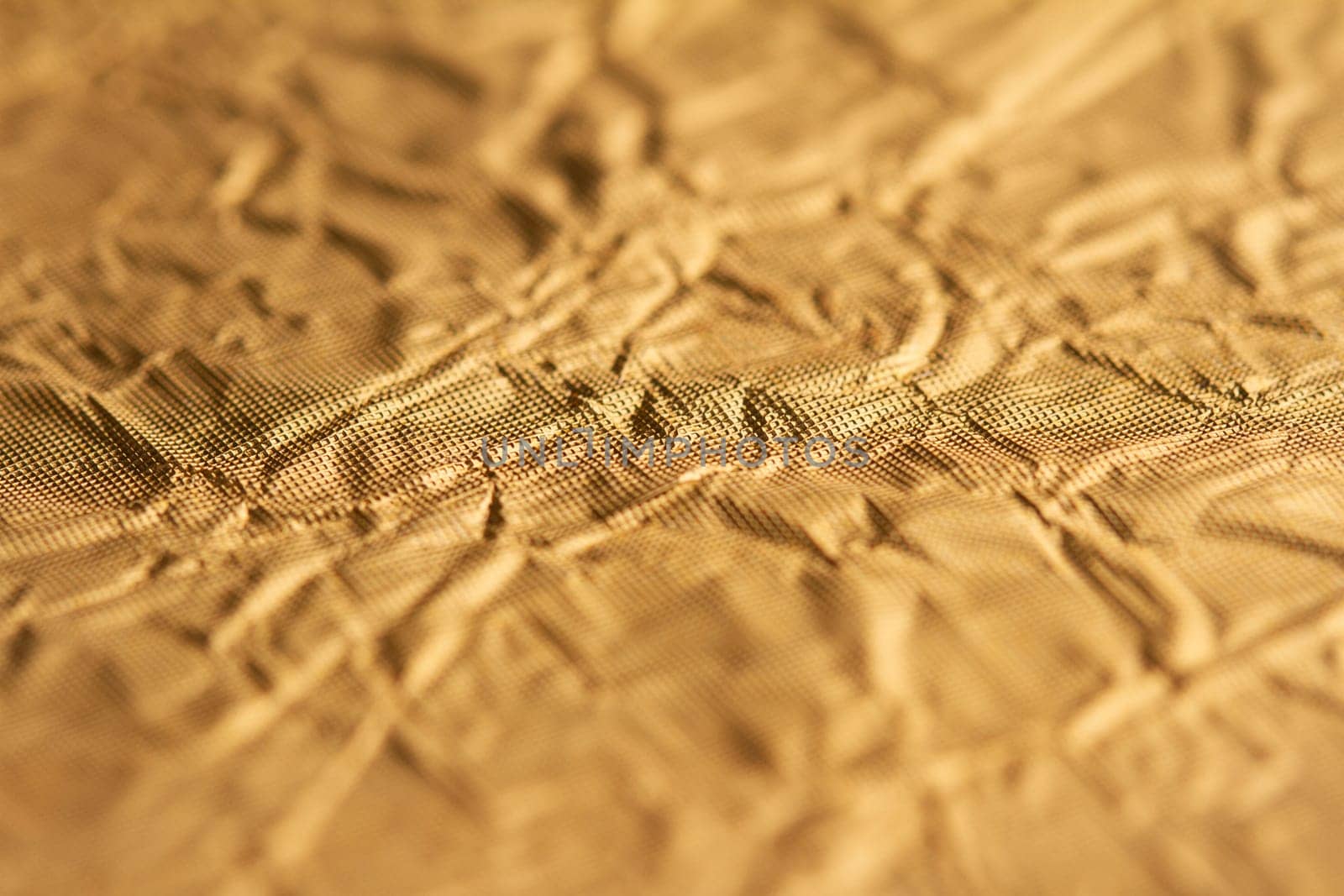 top view detail closeup of textured wrapping paper gold foil leaf with wrinkled surface and shallow depth of field