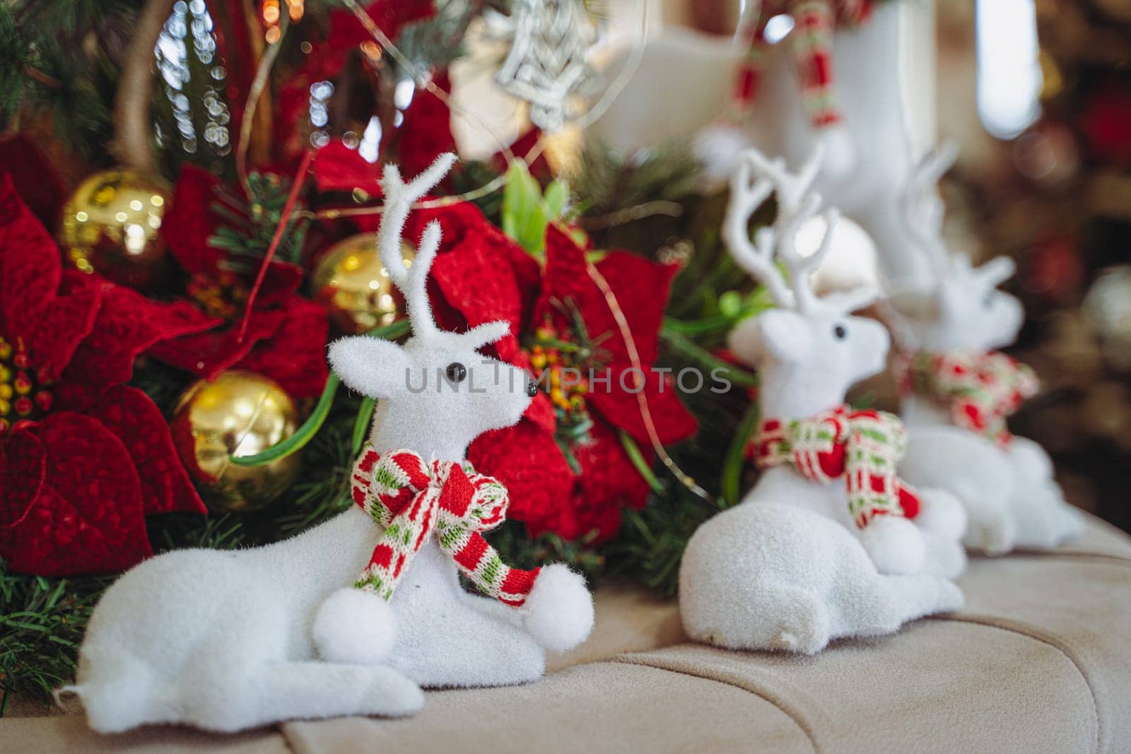 closeup front view of Christmas festive decoration with white plush textile reindeers wearing warm red scarfs and globes  near the fir tree