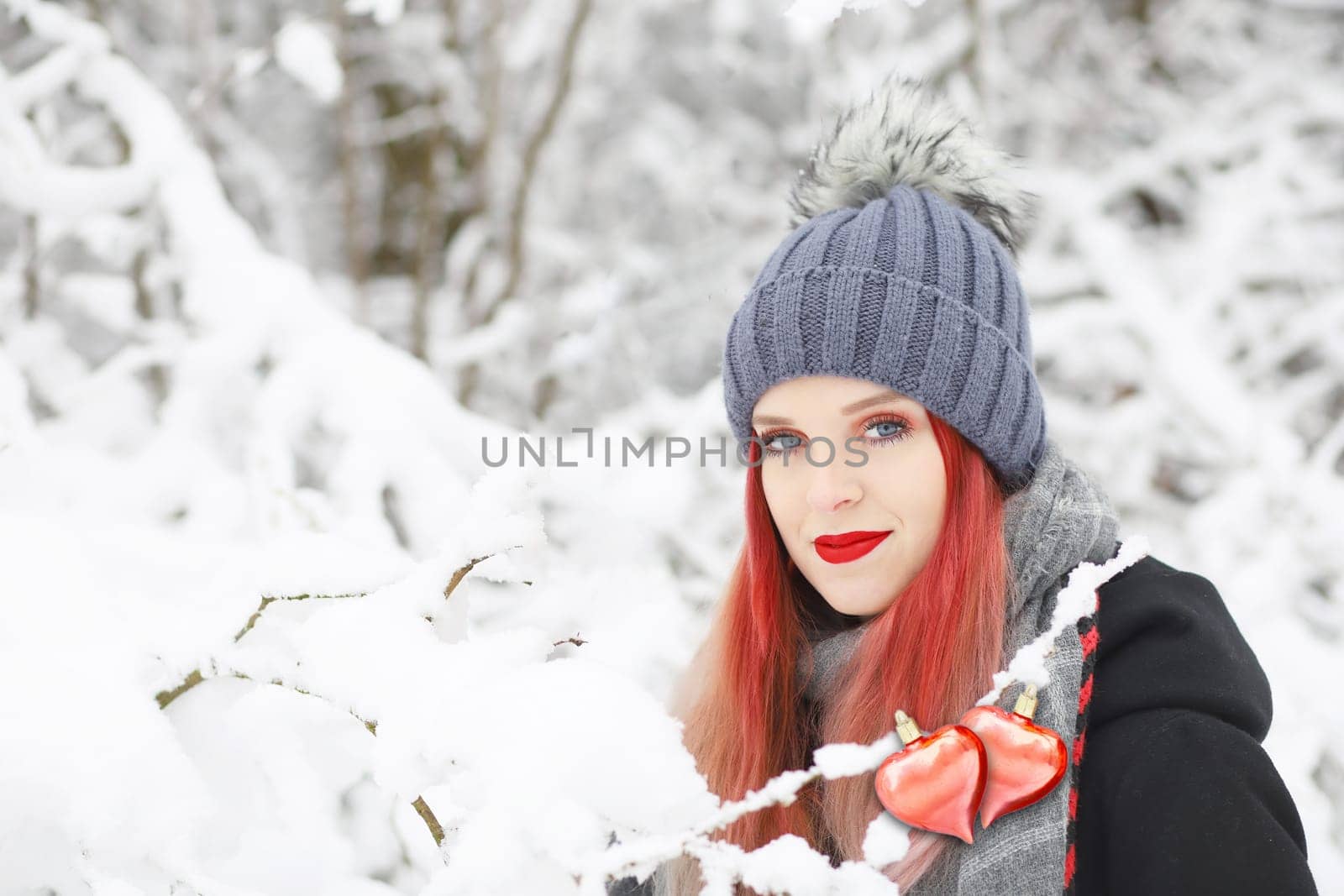 Attractive red hair girl is posing with  with two connected red hearts in the snowy nature.