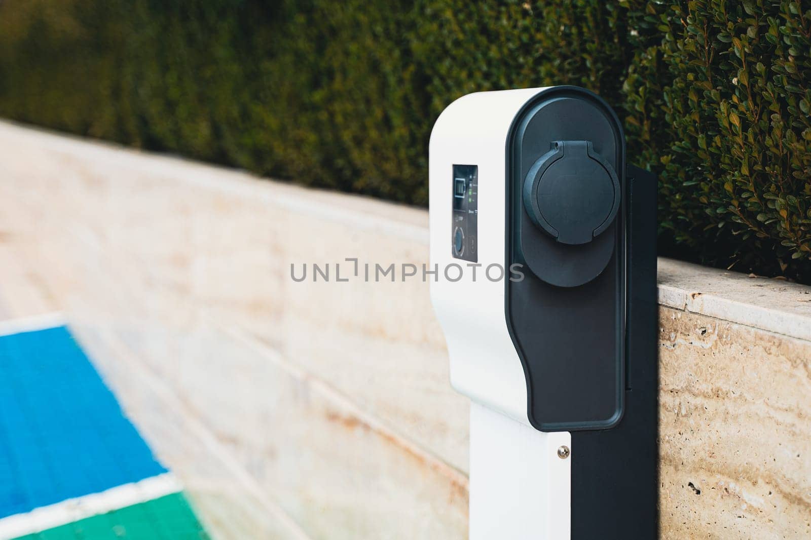 closeup perspective view of vacant electric car charger near a stone wall in parking lot