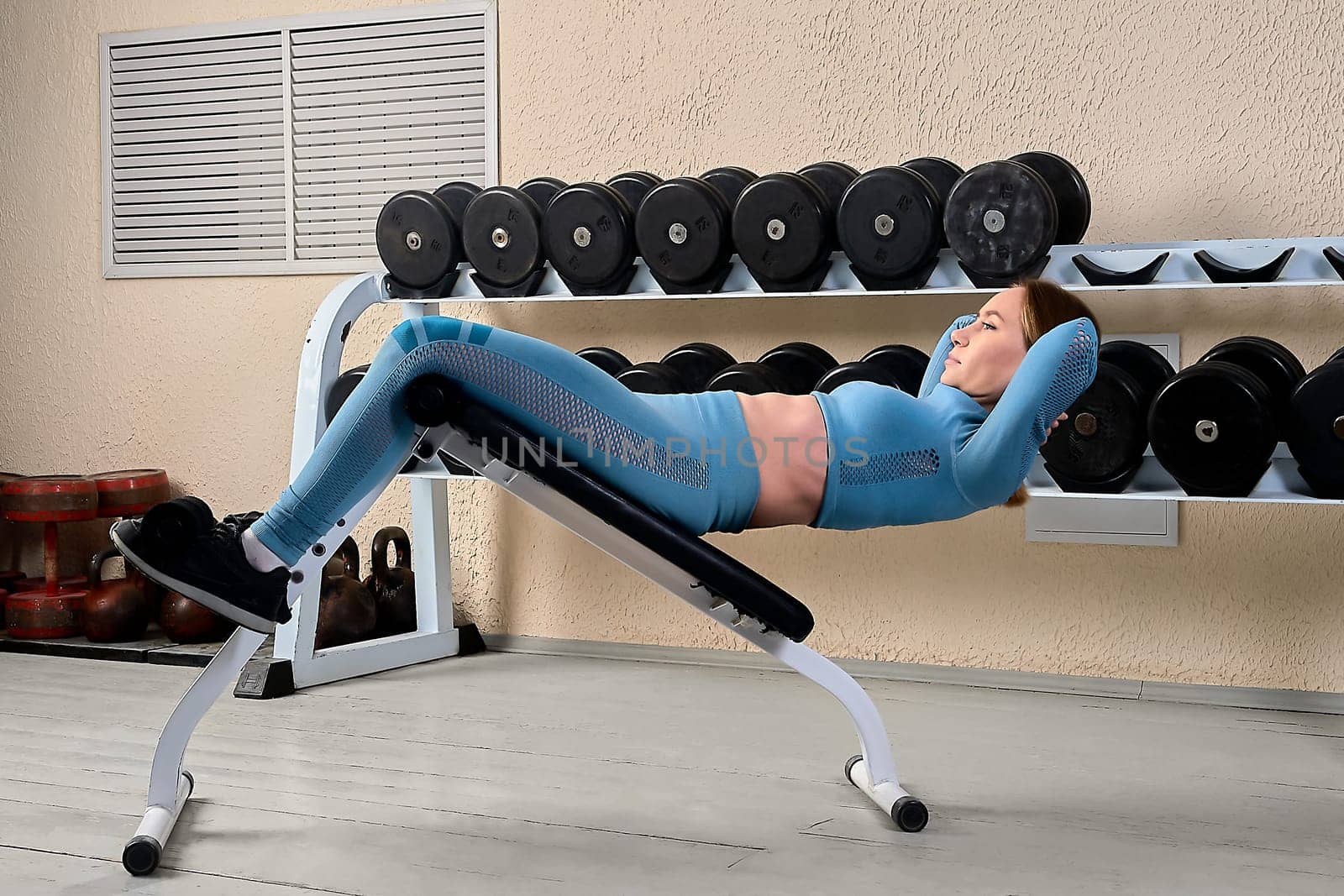 A beautiful young woman shakes her abs on a bench in the gym. High quality photo