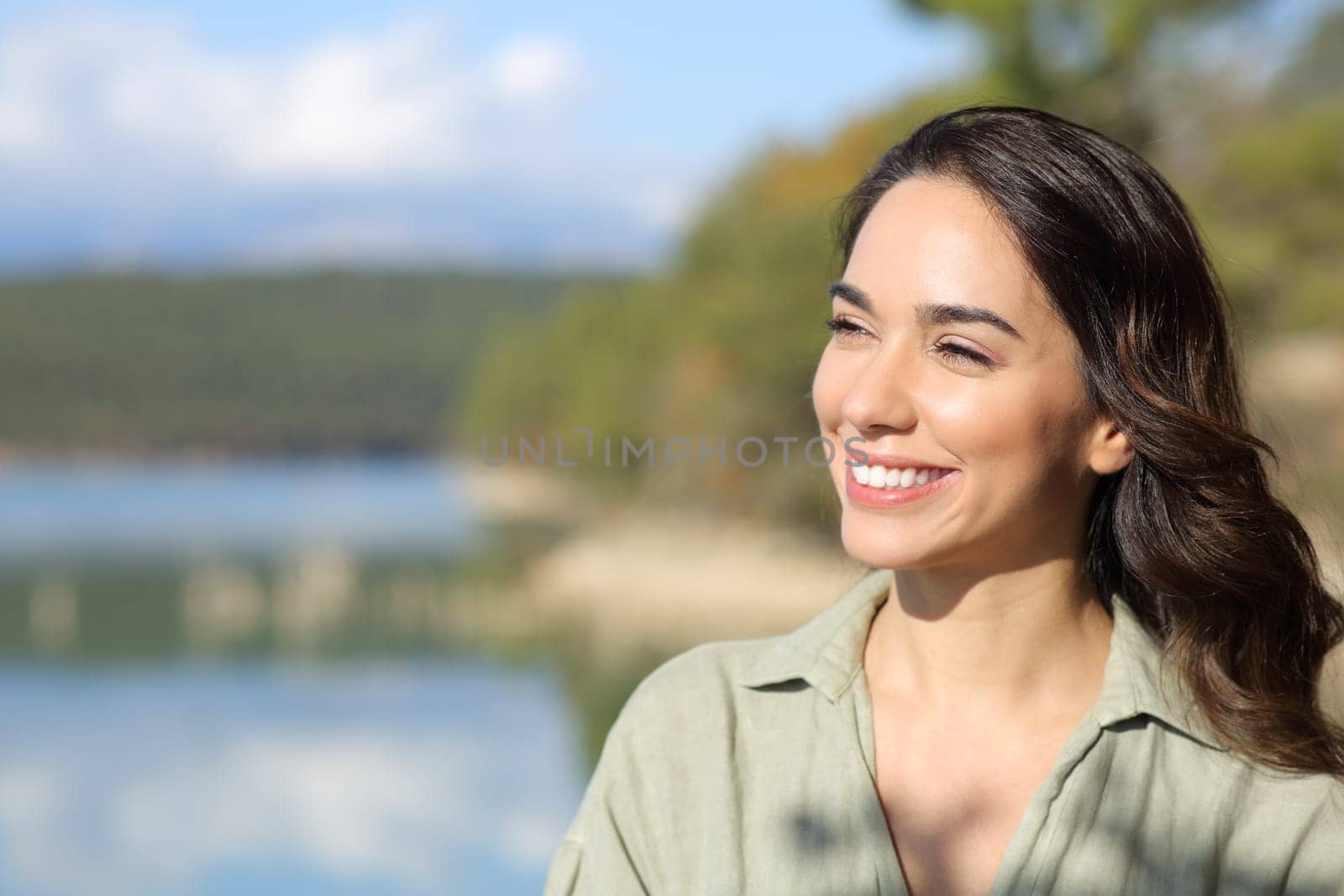Happy woman smiling looking away in a beautiful lake on vacation