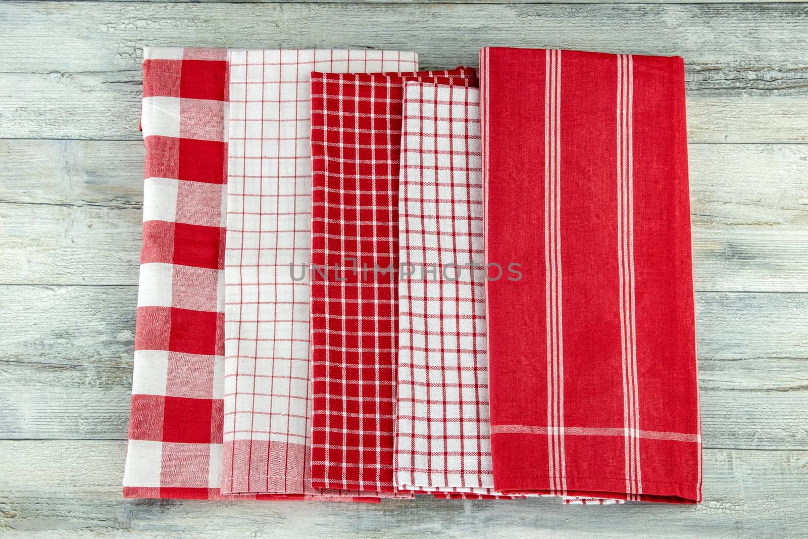 Top view of a set of empty red and white checkered and striped kitchen cloth, textile, tablecloth or napkin on rustic bright wooden table. Template for product display montage.