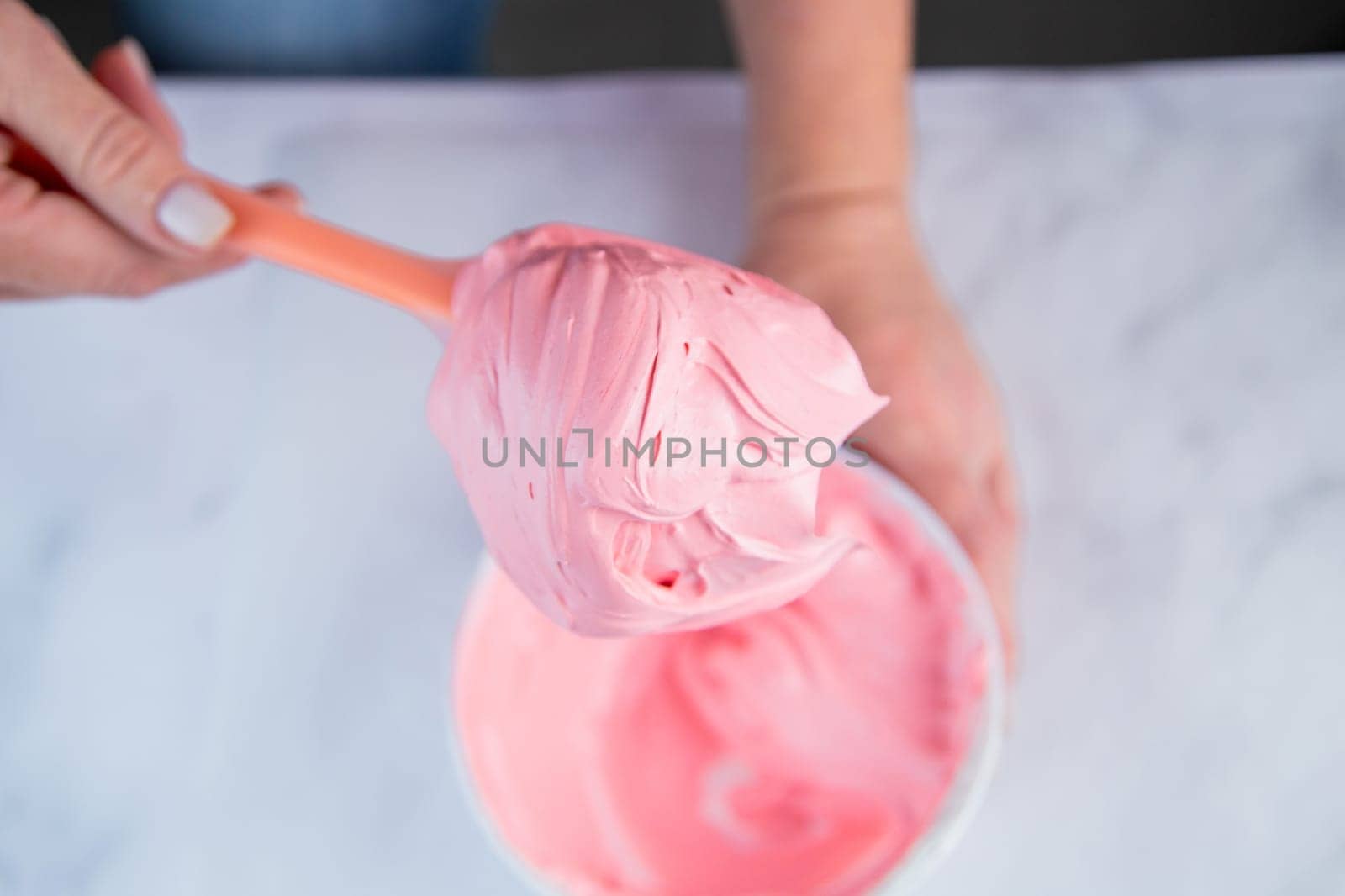 Pink confectionary meringue marengo is mixed in a white bowl on a white marble background by the hands of a pastry chef. High quality photo