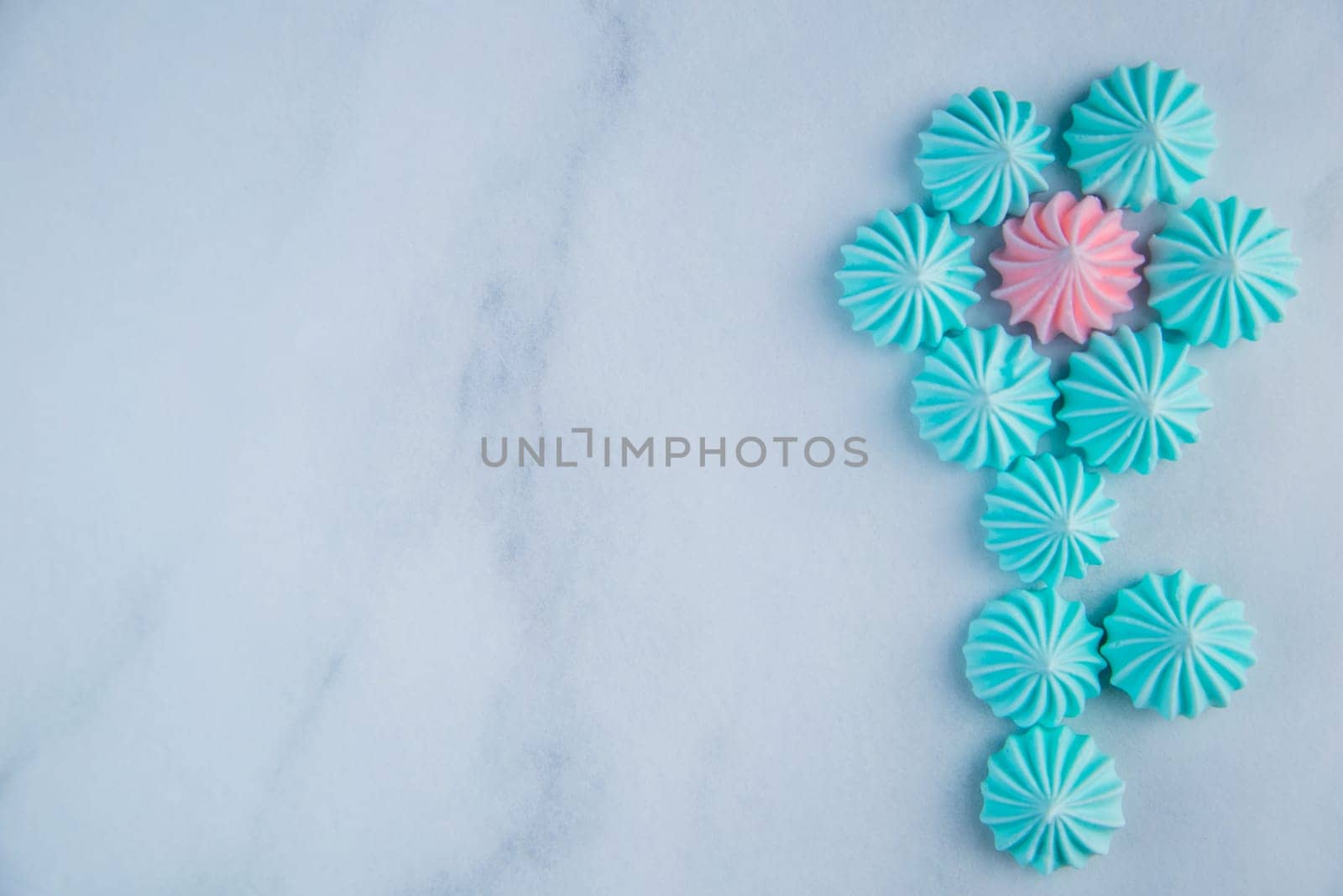 A flower with turquoise petals and a pink core with a stem made of meringue bizet lie on a light marble background with a place for text. High quality photo