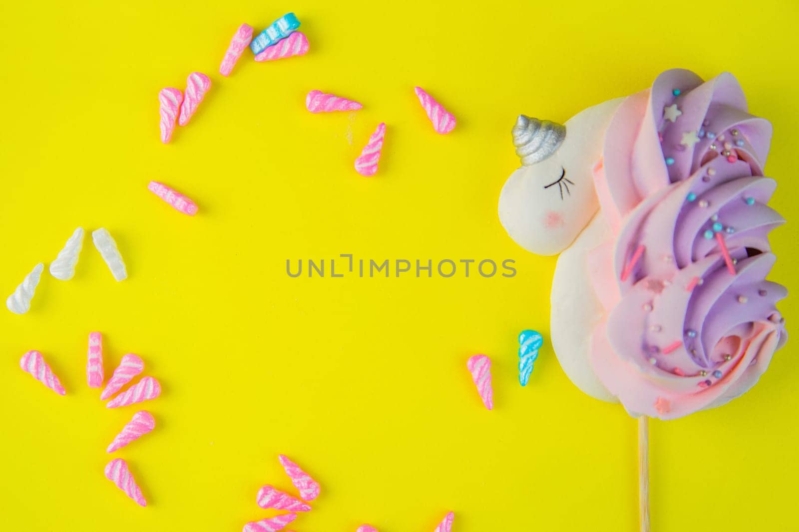 A bizet unicorn is white with a pink-purple tail and a silver horn lying on the side of a bright yellow background, multicolored horns are scattered around the circle, there is a place for text in the middle. High quality photo