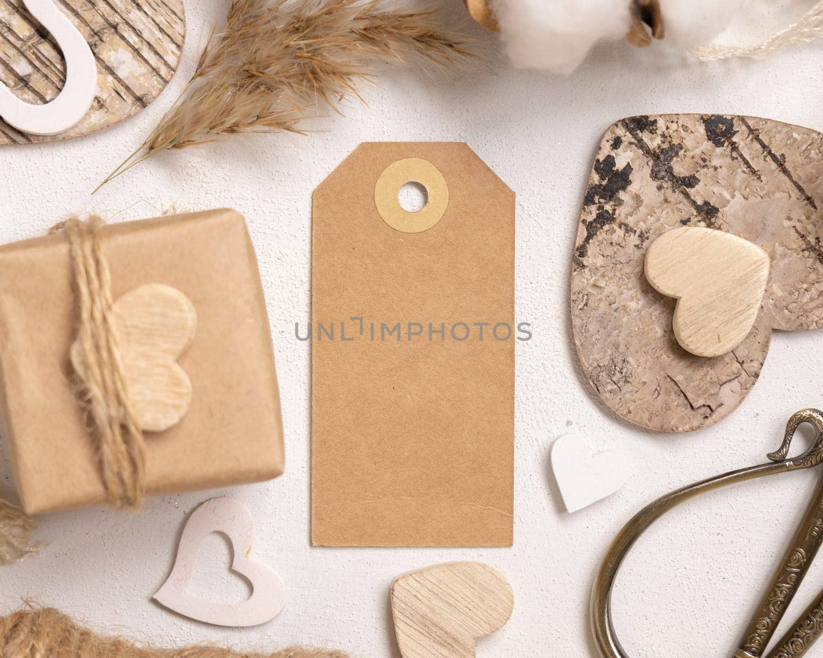 Kraft paper gift tag between Valentines present, wooden hearts and dried flowers top view. Spring scene with vertical blank label. Rustic, cottage chic or bohemian mockup, copy space