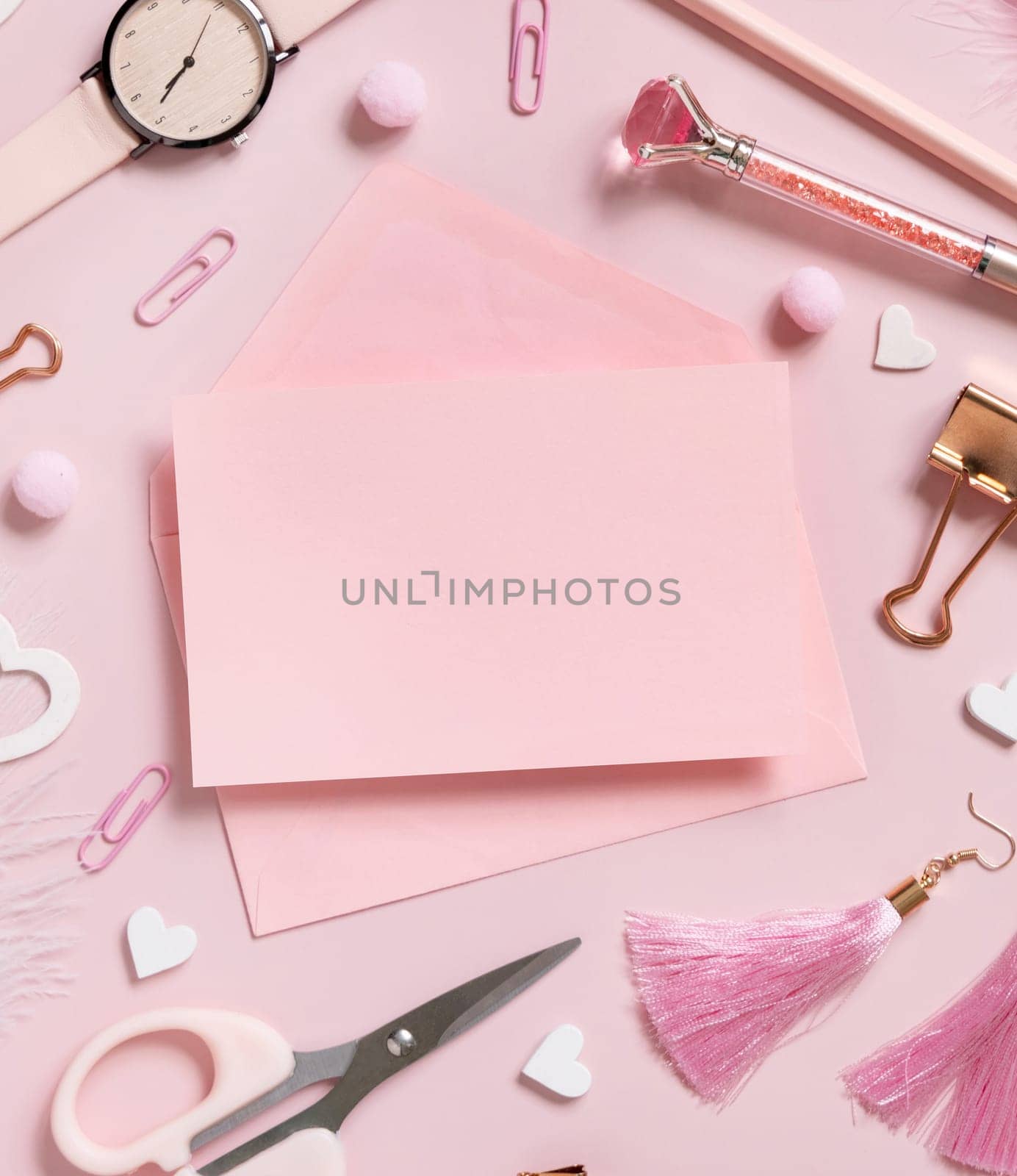 Pink paper card with envelope, school accessories and hearts on pastel pink top view, blank card mockup. Girly workplace. Back to school and valentines day concepts