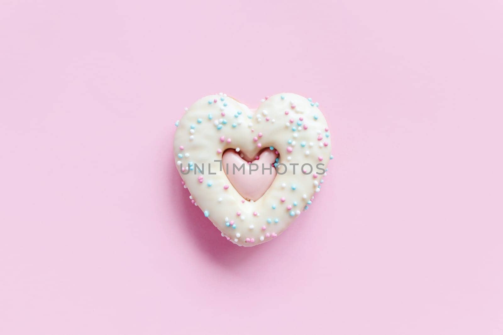 Flat lay of heart shaped gingerbread cookie with sprinkles and icing on pink background. Top view of tasty Valentine's Day bakery, homemade bakery for romantic holiday