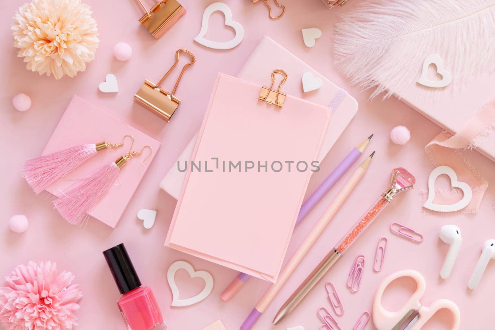 Pink paper card with clip, school girlish accessories and hearts on pastel pink top view, blank card mockup. Girly workplace. Back to school and valentines day concepts