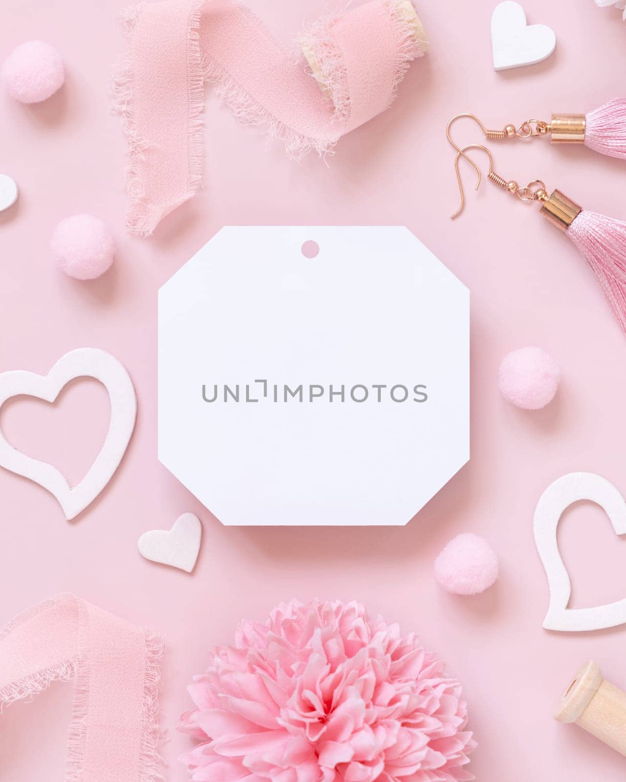 Blank paper gift tag, hearts, flowers, silk ribbons and tassel earrings on pink top view. Romantic scene with blank label mockup flat lay. Valentines day, wedding and girly concept.