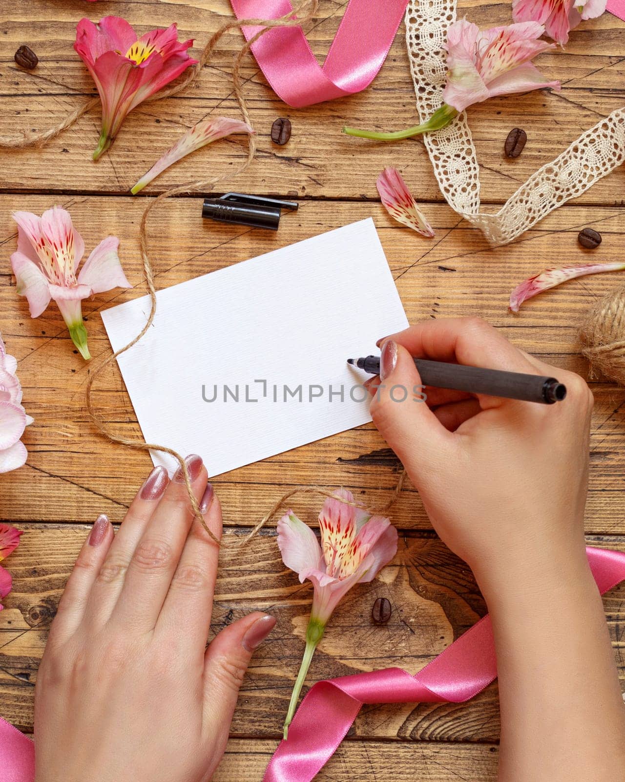 Hands Writing a card on a wooden table between pink flowers top view