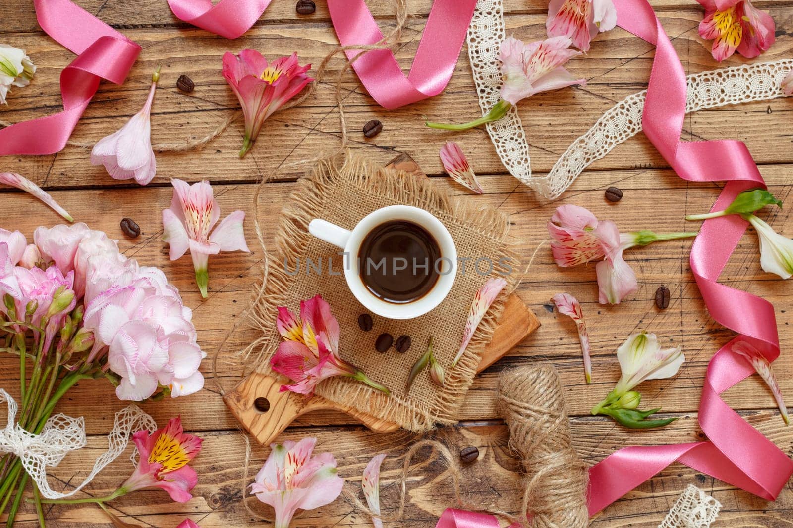 Coffee cup, ribbons, petals and pink flowers on wooden table top view. Romantic breakfast, Spring and valentines day flat lay