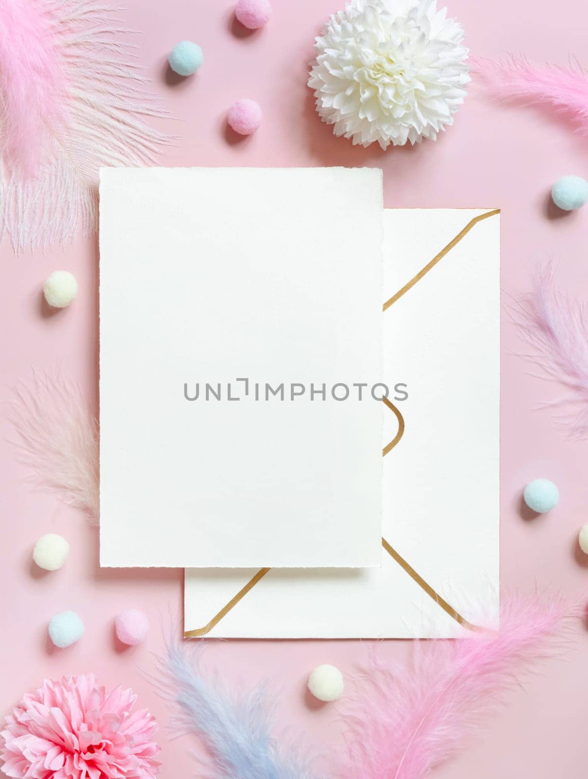 Blank card and envelope near pastel flowers, pom-poms and feathers near ring in a gift box on pink top view. Romantic scene with wedding stationery, place for text flat lay. Valentines, Spring or girlish concept