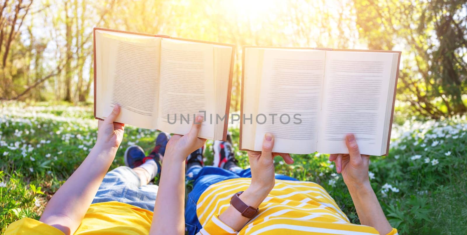 Mother and her son lying down on the beautiful spring field in the sunny park. Concept of the interesting of literature and family leisure.