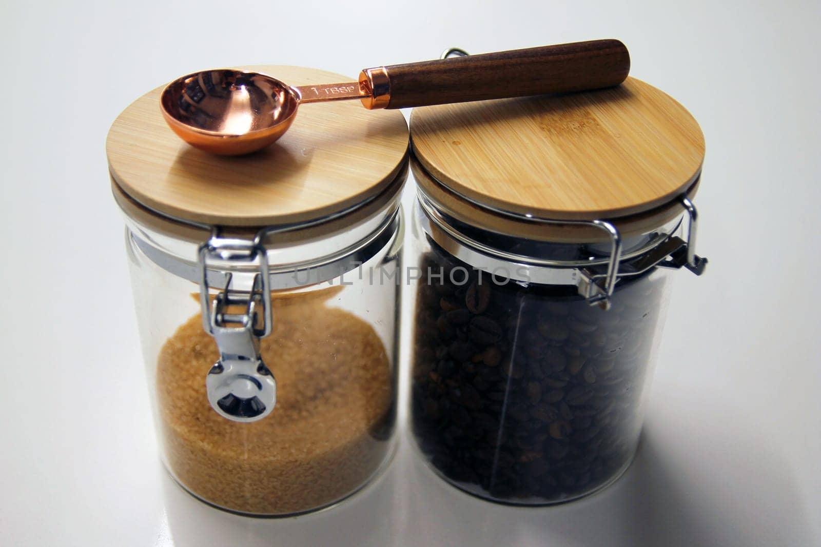 Close up of Two isolated glass and wood jars containing coffee and cane sugar with a copper and wood table spoon