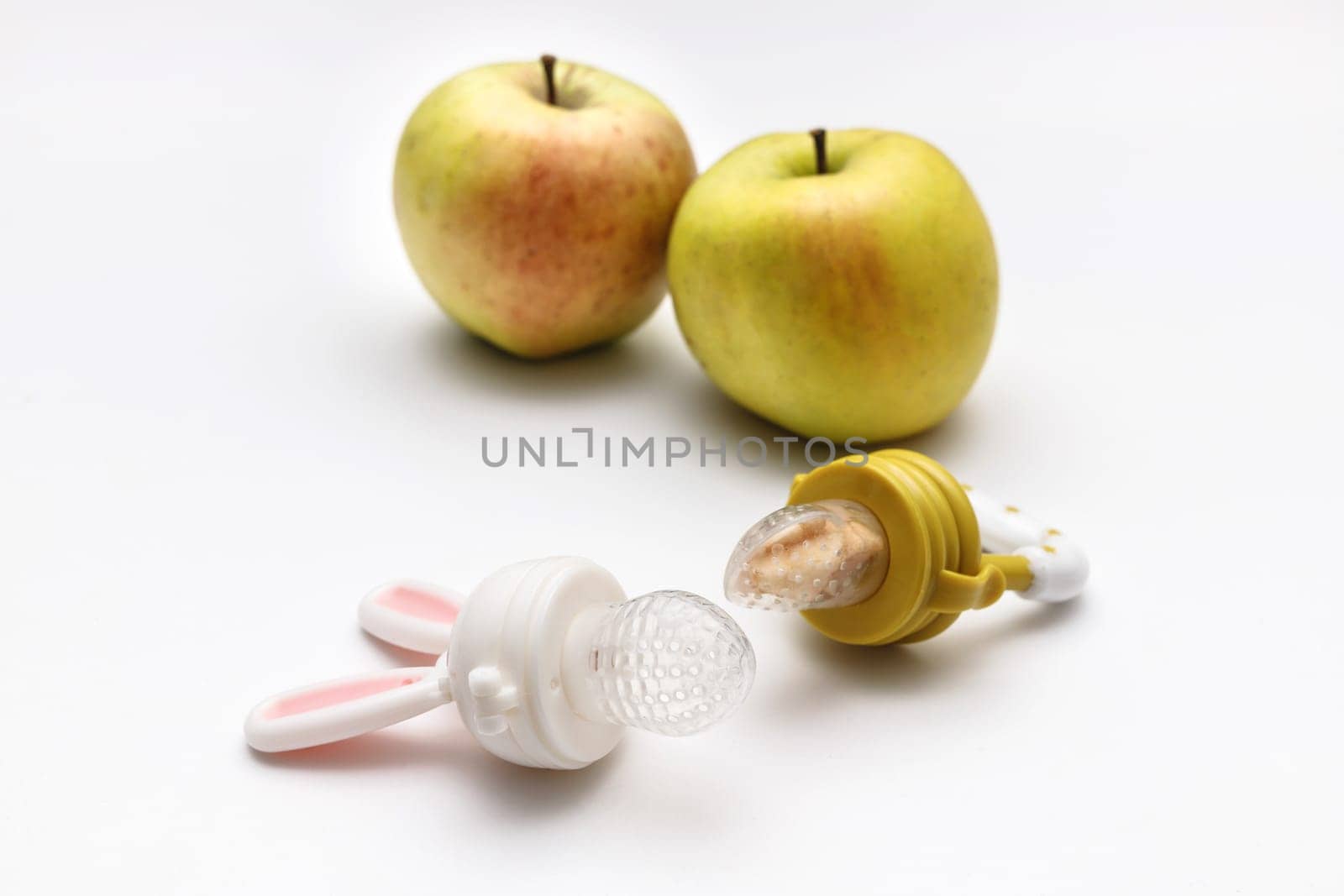 Nibbler with fresh apples on white table, closeup. Baby feeder.