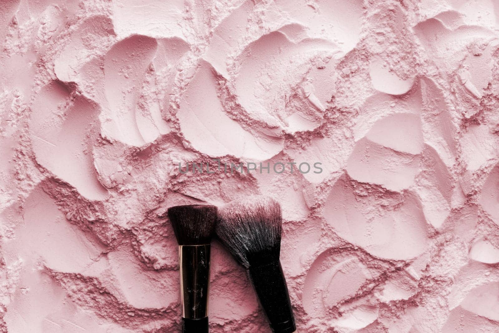 Makeup brushes on pink cosmetic powder background. Flat lay, top view.