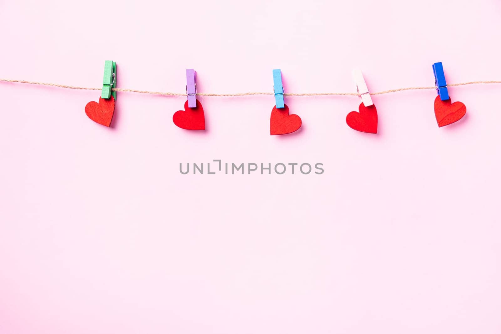 Happy Valentine's day concept. red heart-shaped valentines decoration hanging with wood clips for love on the rope isolated on pink background with copy space