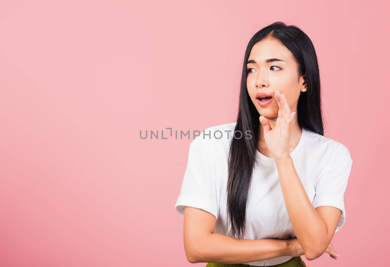 Asian happy portrait beautiful cute young woman teen standing hand on mouth talking whisper secret rumor studio shot isolated on pink background, Thai female looking to side away with copy space