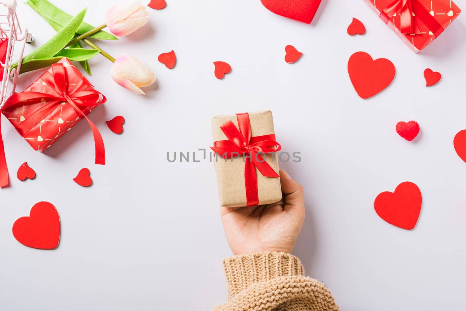 Valentine's day and birthday. Woman hands holding gift or present box decorated and red heart surprise on white background, Female's hand hold gift box package in craft paper Top view flat lay