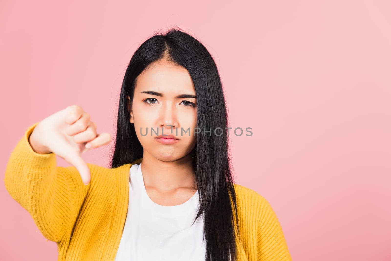 Portrait Asian beautiful young woman unhappy, negative gesture showing finger thumbs down or dislike sign, studio shot isolated on pink background, Thai female rejection unlike with copy space