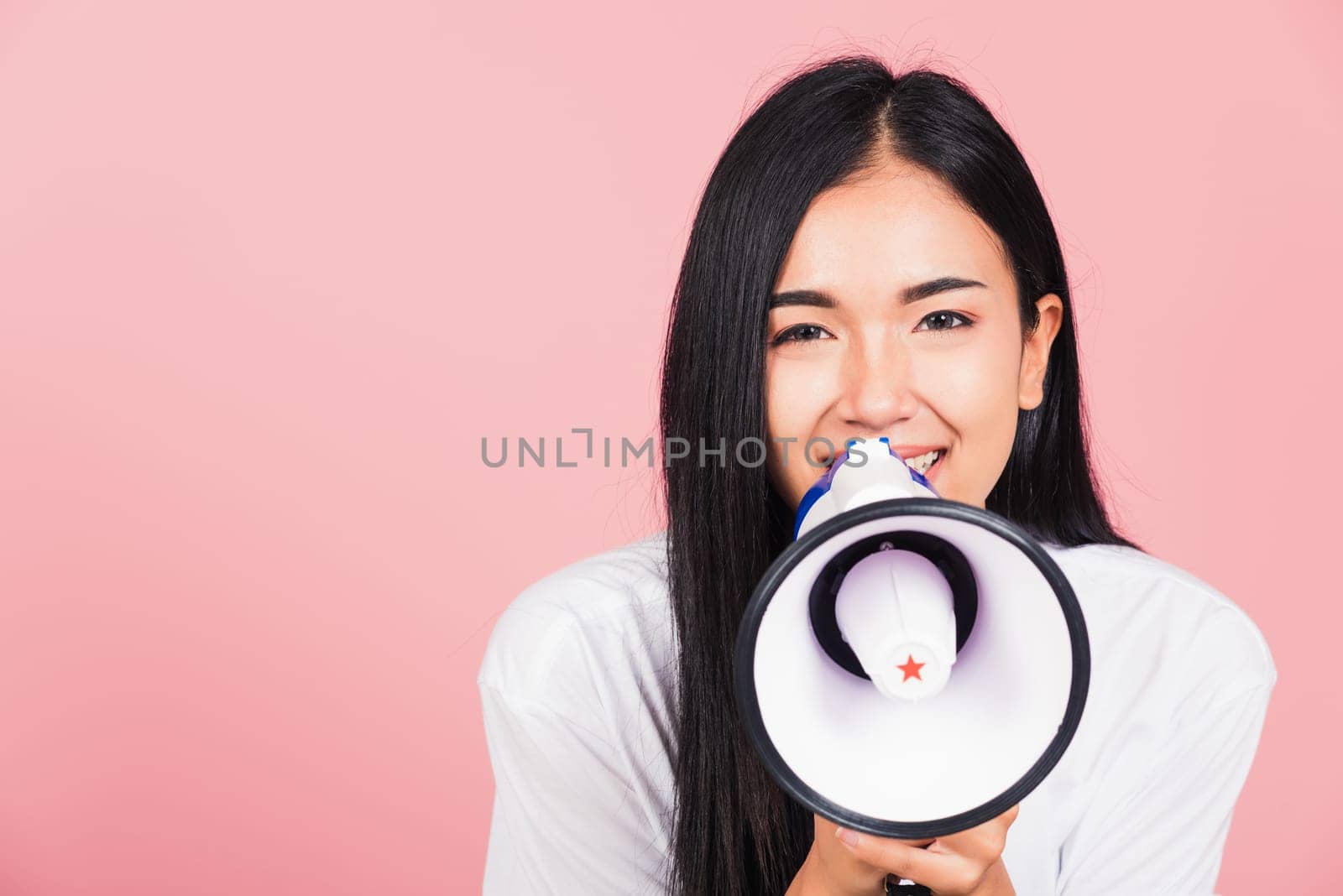 Portrait of happy Asian beautiful young woman teen confident smiling face holding making announcement message shouting screaming in megaphone, studio shot isolated on pink background, with copy space