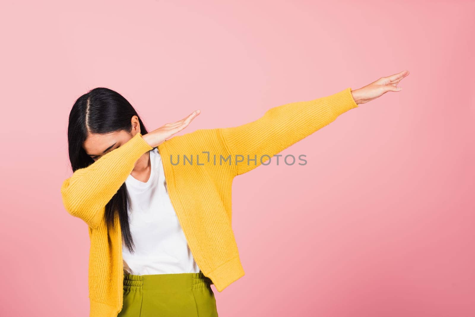 Asian happy portrait beautiful cute young woman teen smile standing move showing DAB dance against gesture raise hands arms covering  face isolated, studio shot on pink background with copy space