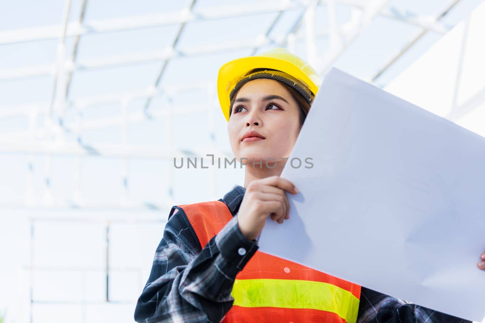 Asian engineer architect worker woman holding blueprint infrastructure progress at construction site, engineering female leader standing hold paper plan control worker to building project
