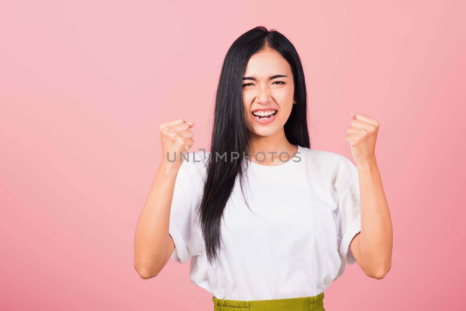 Asian happy portrait beautiful cute young woman standing angry and mad raising fist frustrated and furious while shouting with anger isolated, studio shot on pink background and copy space