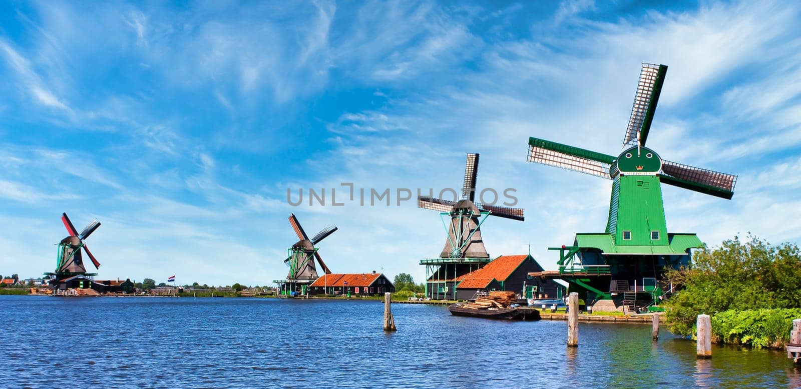 ZAANSE SCHANS, NETHERLANDS - CIRCA AUGUST 2020: Dutch windmill in green countryside close to Amsterdam, with blue sky and river water.
