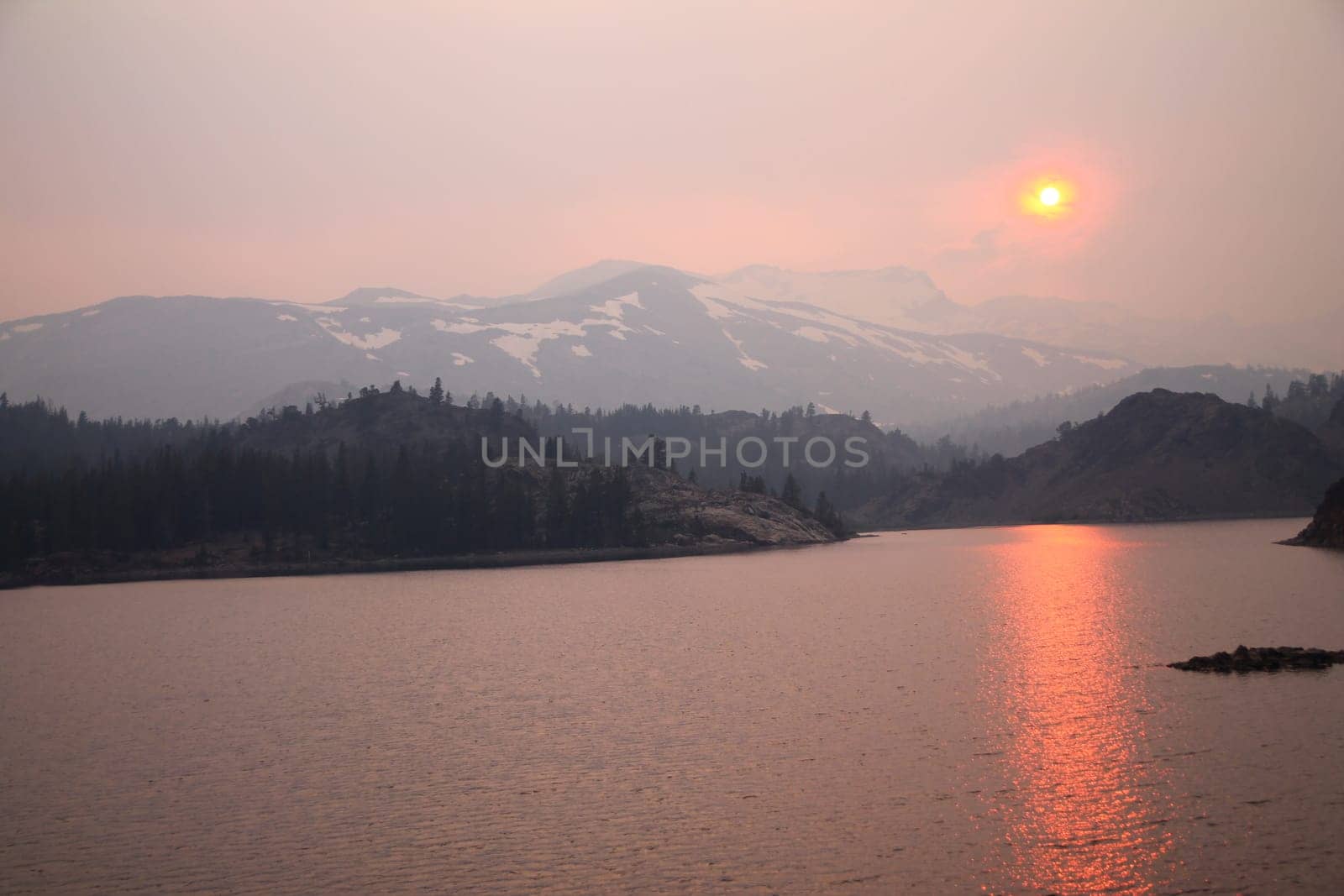 The sun reflecting on the lake through the fog and the ash of a wildfire in Yosemite National Park in California