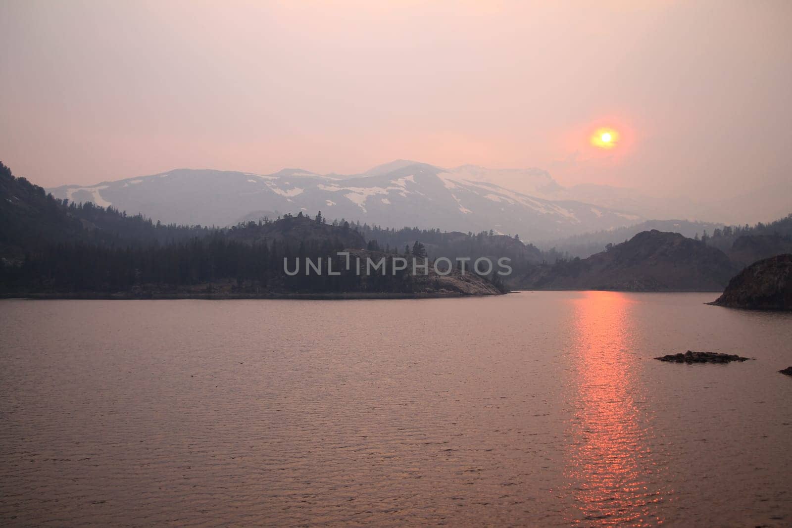 The sun reflecting on the lake through the fog and the ash of a wildfire in Yosemite National Park in California