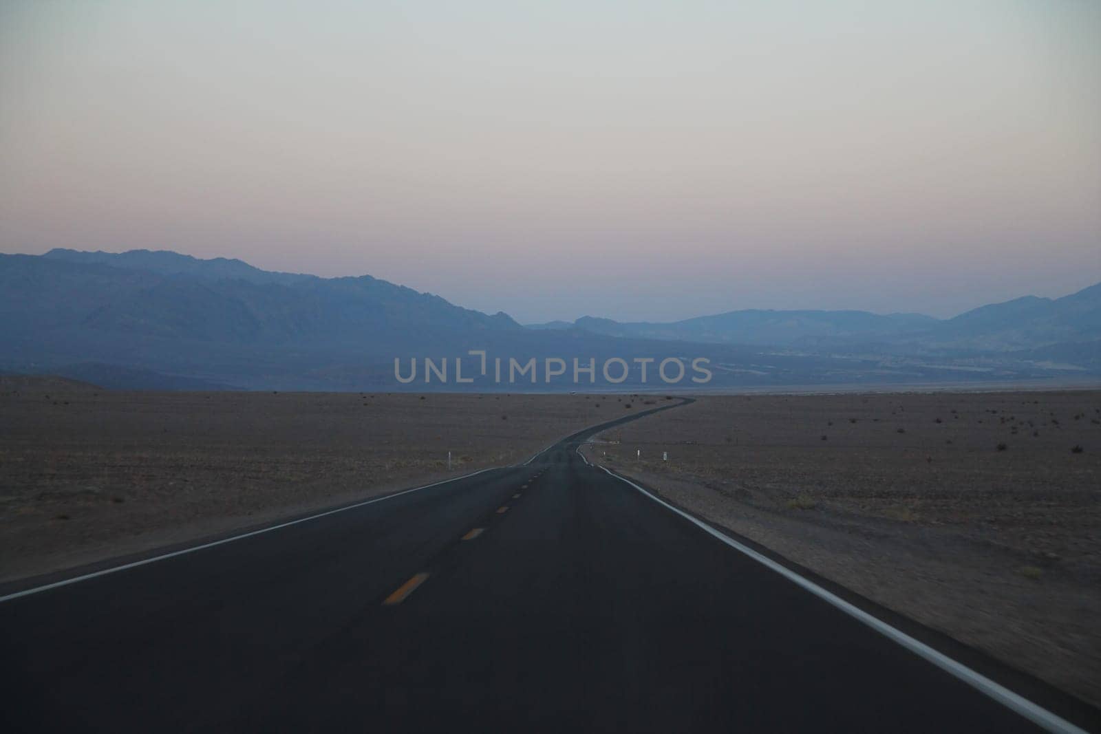 The never ending road during the dusk of a sunset in the Death Valley desert in California