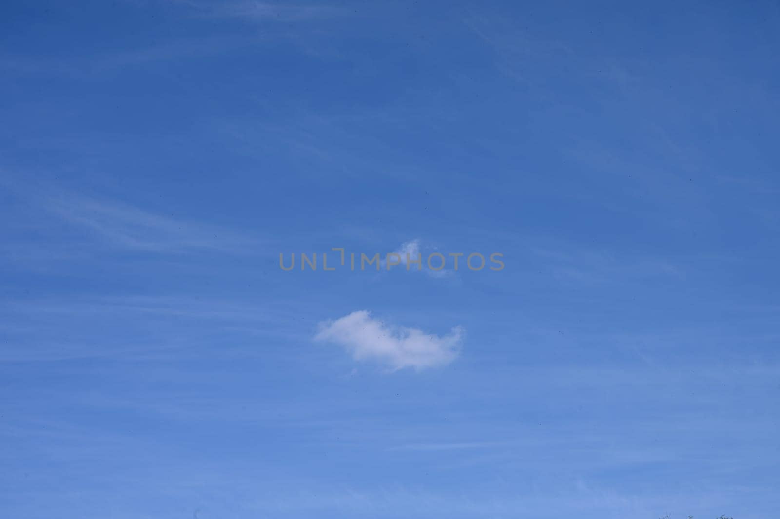 Soft clouds float effortlessly against a clear blue sky on a tranquil afternoon, creating a peaceful ambiance.