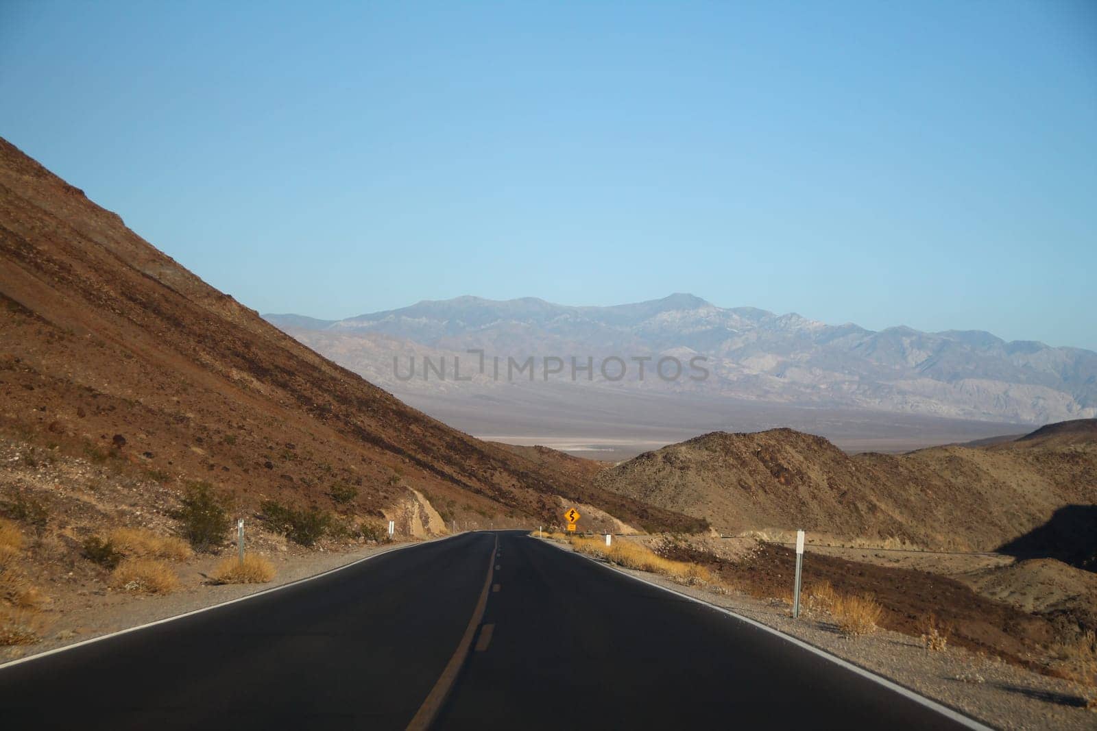 The black asphalt road with the mountains of the left and on distance in California